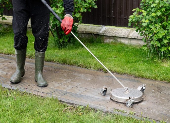 Professional paving stone cleaning. Cleaning a stamped concrete patio with a pressure washer in a residential garden during the day Professional paving stone cleaning. Cleaning a stamped concrete patio with a pressure washer in a residential garden during the day